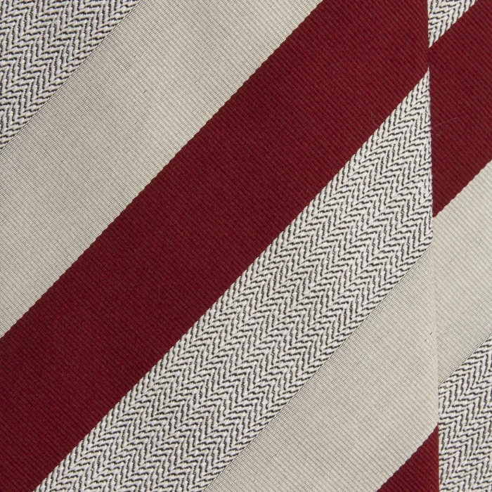 A close-up of a red silk jacquard tie in cream stripes with a herringbone band