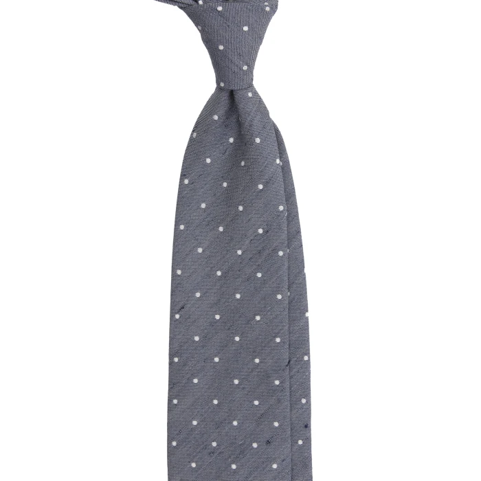 A grey-blue silk jacquard tie with white polka dots, tied in a knot