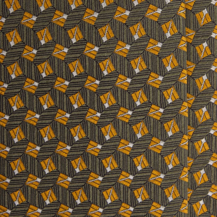 A close-up of an olive silk jacquard tie with a small geometric pattern